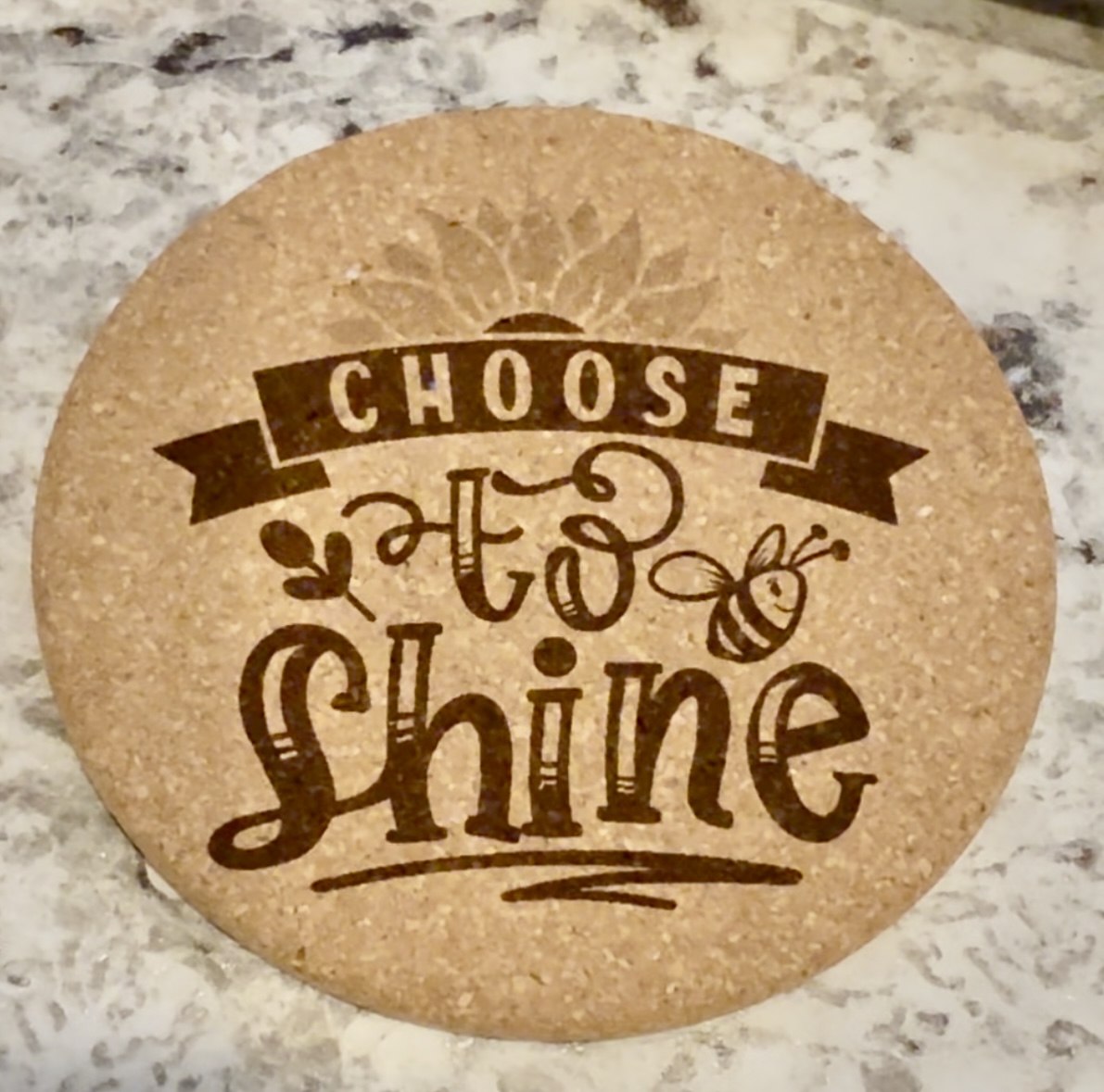 Laser-engraved cork coaster reading 'Choose to Shine' with a sunflower and bee design