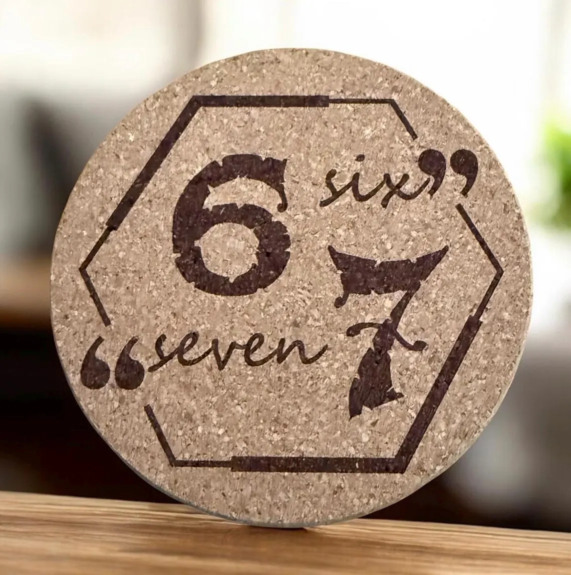 Round cork coaster laser engraved with '6 7' in a hexagon design