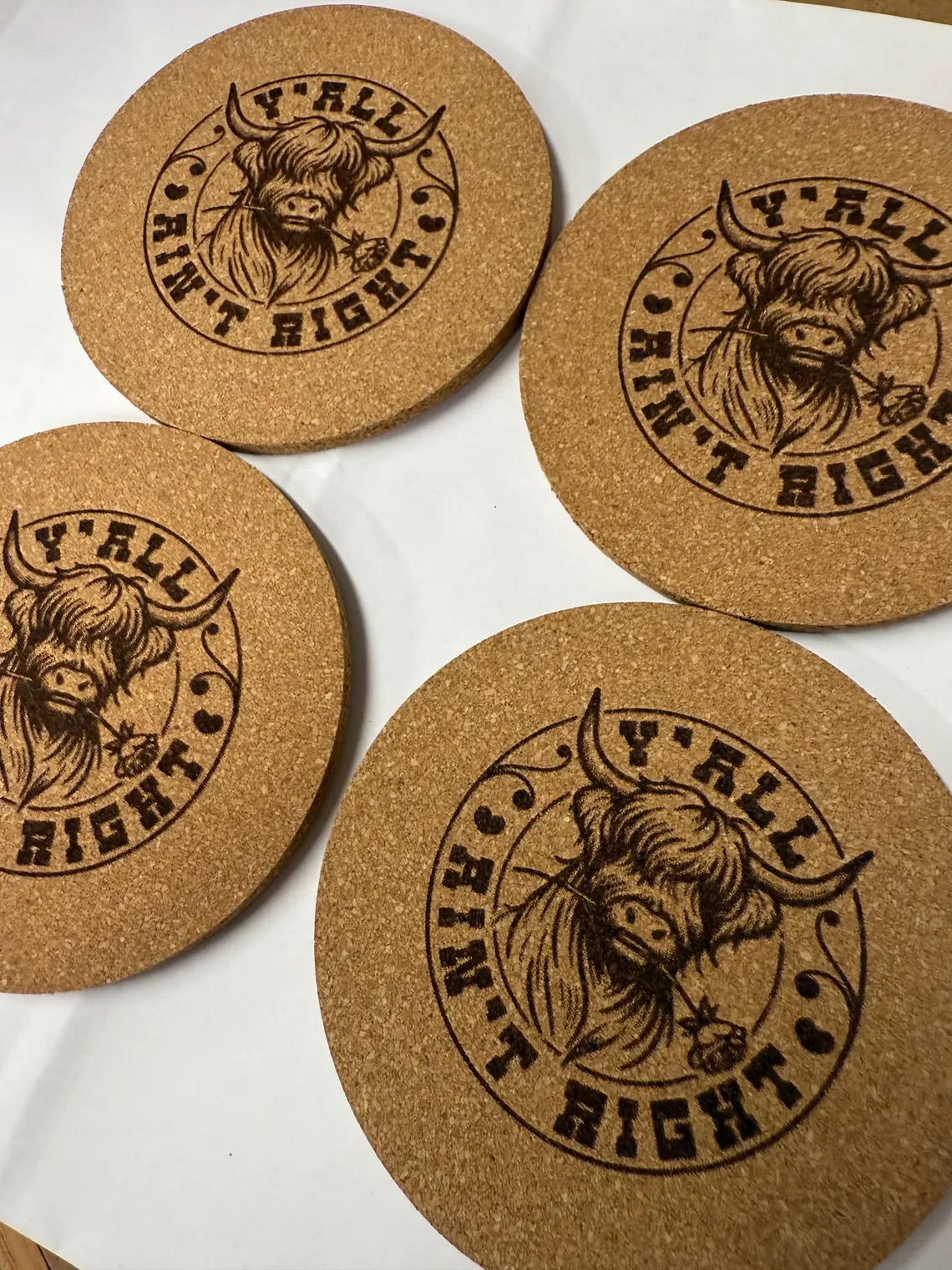 Round cork coasters laser engraved with a highland cow and 'Y'all Ain't Right' lettering